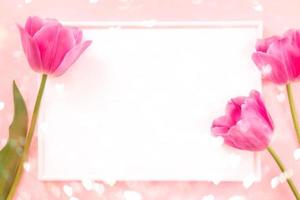 marco blanco y tulipanes rosas en rosa pastel con corazones de luces bokeh. vista superior, espacio de copia, maqueta. foto