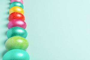 Row of brightly multicolored painted Easter eggs on trendy Neo Mint pastel backdrop. Selective focus. Perspective view. photo