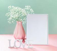 Creative card with gypsophila in vase, empty white frame, white letters LOVE on pastel pink-green. photo