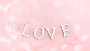 White letters LOVE on pastel pink with bokeh lights hearts. Festive background. Top view, flat lay. photo