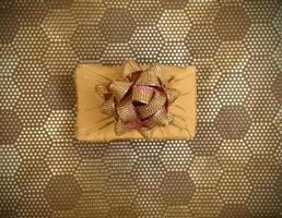 caja de regalo de vista superior, envuelta en tela amarilla en técnica furoshiki sobre fondo dorado con patrón hexagonal de puntos. foto