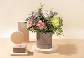 Eco friendly monochrome composition with flowers bouquet and wooden stands with DIY gift box on beige with shadows. photo