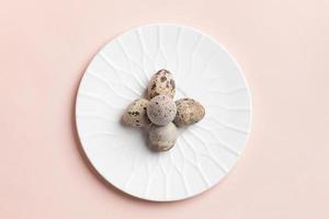 Minimal Easter image with quail eggs laid out as cross on white plate on pastel pink background. photo