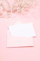 Pastel pink festive greeting card with empty white sheet in envelope and white gypsophila flowers. Copy space for text. photo