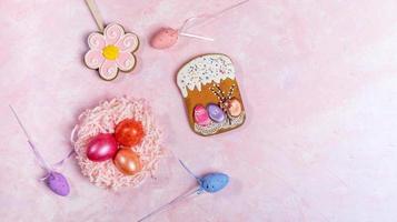 Easter festive background with color eggs in nest, decorative eggs and Easter gingerbreads on pink backdrop. Top view. photo