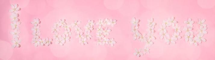 Wide festive banner. Inscription I LOVE YOU laid out from flowers of white apple tree on pink backdrop with bokeh. photo