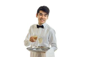 Cheerful man waiter in uniform and bowtie with glasses of white wine on silver tray smiling photo