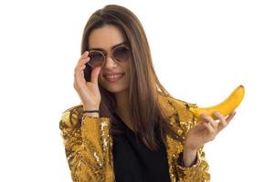 Portrait of chic young girl in glasses with a banana in her hand isolated on white background photo