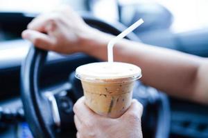 la conductora asiática sostiene una taza de café con hielo para beber en el automóvil, es peligrosa y corre el riesgo de sufrir un accidente. foto