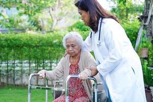 Doctor help Asian elderly woman disability patient walk with walker in park, medical concept. photo