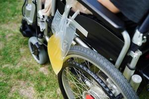 Asian disability woman with urine bag on wheelchair.