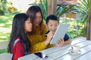 Mother teaching her son and daughter learning online on tablet in the living corner outside the house. Concept adult teaching children, family, learning outside the classroom, outside activities. photo