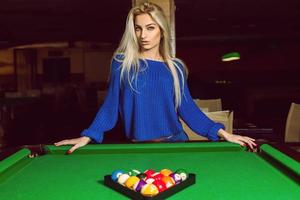 Lovely adult blonde posing near a billiard table with a pyramid of balls photo