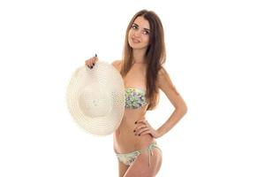 portrait of attractive slim young woman in swimsuit with floral patter looking away with straw hat in her hands isolated on white background photo