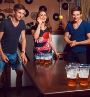 Beautiful brunette girl having fun with twins playing beer pong photo