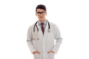 Un joven y apuesto doctor posando con uniforme y gafas aisladas de fondo blanco en el estudio foto