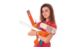 portrait of young attractive brunette building woman in red uniform with tools in hands makes renovation and looking at the camera isolated on white background photo