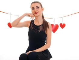 beautiful girl in a black dress and red lipstick looks up smiling and standing near the Ribbon with hearts photo