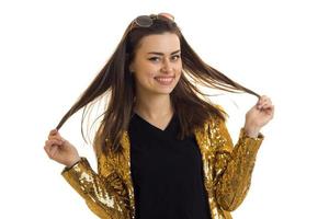 smiling beautiful brunette in gold shiny jacket keeps hands hair and looks into a camera photo