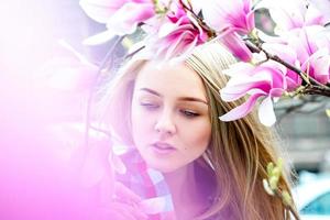 hermosa joven rubia con ojos azules posando cerca de flores rosas florecientes foto