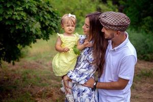 primer plano retrato de una hermosa familia joven que lleva a una pequeña y elegante niña en el parque verde foto