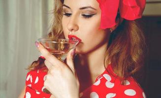 Portrait of young beautiful woman in pinup style drinks martini photo