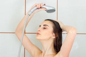 beautiful young girl stands under the shower closing her eyes and washes her head photo