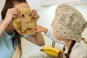 cute little homecook girl with her beautiful mother makes pancakes in white kitchen. photo