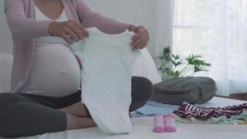 as mulheres grávidas escolhem roupas para recém-nascidos. as mulheres estão preparando roupas e acessórios necessários para o dia do parto. conceito de preparação antes de dar à luz. video