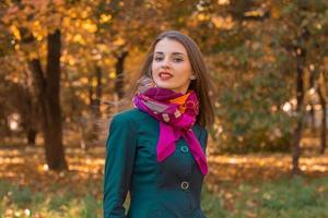 hermosa chica con un pañuelo rosa alrededor del cuello se encuentra en el parque de otoño foto