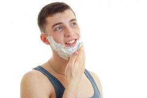 Cheerful young man with foam on dace smiling and looking away photo