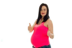 feliz futura madre embarazada con camisa rosa mostrando los pulgares hacia arriba con dos manos aisladas de fondo blanco foto