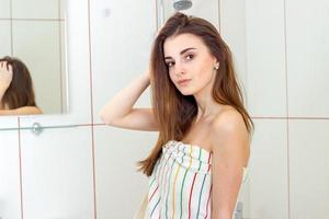 a charming young girl stands in the bathroom in a towel and stares into the camera photo