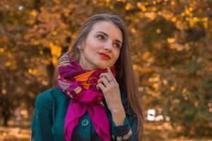 attractive young girl stands in the park with a pink scarf around her neck and looks away photo