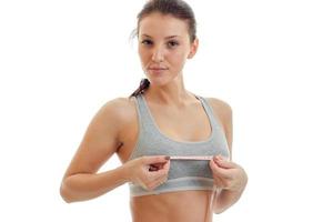 beautiful young girl in grey top looks into the camera and takes the measuring tape chest close-up photo