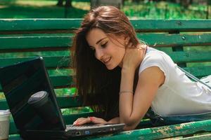 Portrait of smiling beautiful Brunettes with a laptop on the bench photo