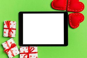 Top view of digital tablet surrounded with gift boxes and hearts on colorful background. Saint Valentine's day photo