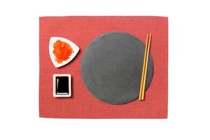 Emptyround black slate plate with chopsticks for sushi, ginger and soy sauce on red napkin background. Top view with copy space for you design photo