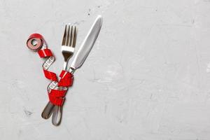 Crossed fork and knife are wrapped in measuring tape on gray background. Concept of diet for weight loss with copy space photo