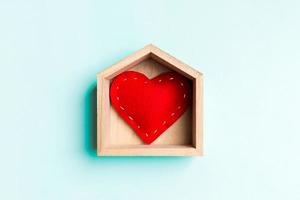 vista superior del corazón textil rojo en una casa de madera sobre fondo colorido. concepto de hogar dulce hogar. día de San Valentín foto