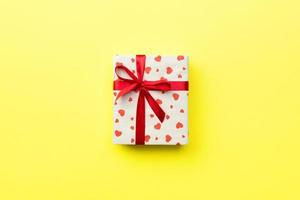 Gift box with red ribbon and heart on yellow background, top view with copy space for text photo