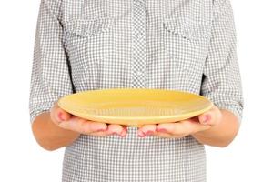 la chica de la camisa a cuadros sostiene un plato amarillo redondo vacío frente a ella. mano de mujer sostenga el plato vacío para su diseño. vista en perspectiva, aislada sobre fondo blanco foto