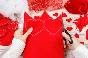 women's hands make red hearts from the fabric. Preparation for St. Valentine's Day. homemade festive decorations. Above view, flat lay photo