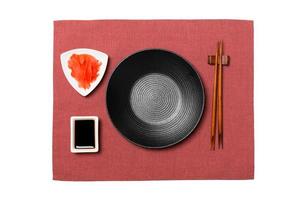 Empty round black plate with chopsticks for sushi and soy sauce, ginger on red napkin background. Top view with copy space for you design photo