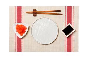 Empty round white plate with chopsticks for sushi and soy sauce, ginger on sushi mat background. Top view with copy space for you design photo