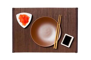 Empty round brown plate with chopsticks for sushi, ginger and soy sauce on dark bamboo mat background. Top view with copy space for you design photo