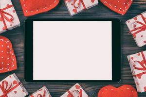 Digital tablet blank screen with gift box and hearts decor on wooden table. Top view. Valentines Day concept background photo