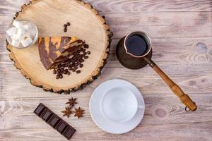 Top view of a piece of chocolate cake on wooden stump with a coffee cup, tea spoon, fork, anise, coffee beans, chocolate bar and bowl with sugar cubes on a wooden background photo