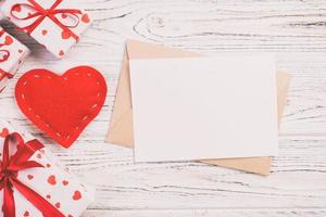 correo de sobre con corazón rojo y caja de regalo sobre fondo blanco de madera. tarjeta de san valentín, amor o concepto de saludo de boda foto