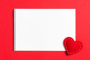 Top view of notebook surrounded with a textile heart on colorful background. Valentine's Day concept photo